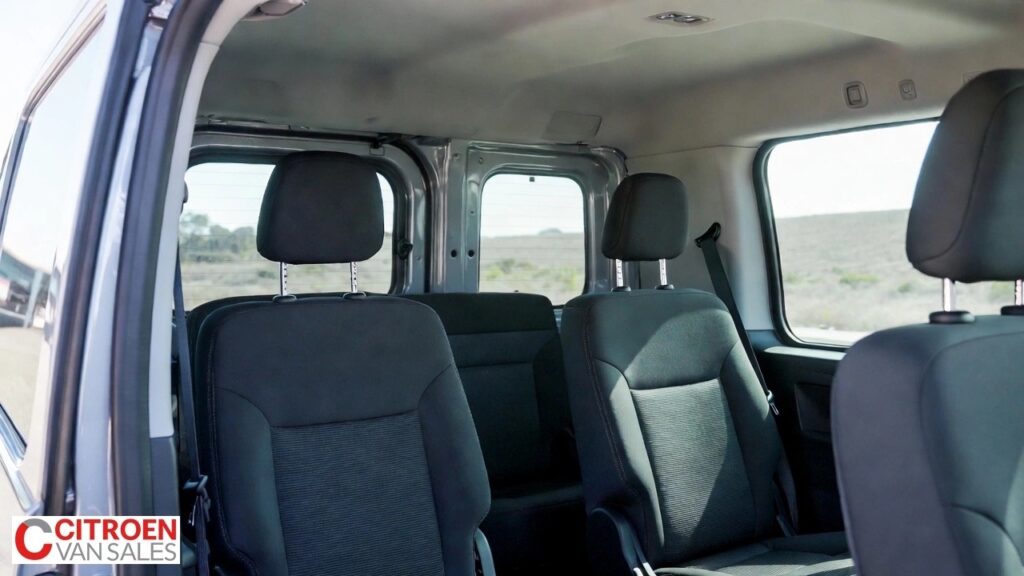 Crew cab van interior showing second-row seats, seatbelts, side windows, and a bulkhead separating the load area.